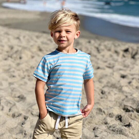 Boy wearing white and blue striped tshirt with tan shorts on the beach Me and henry boys clothing at la dee dah fashion boutique